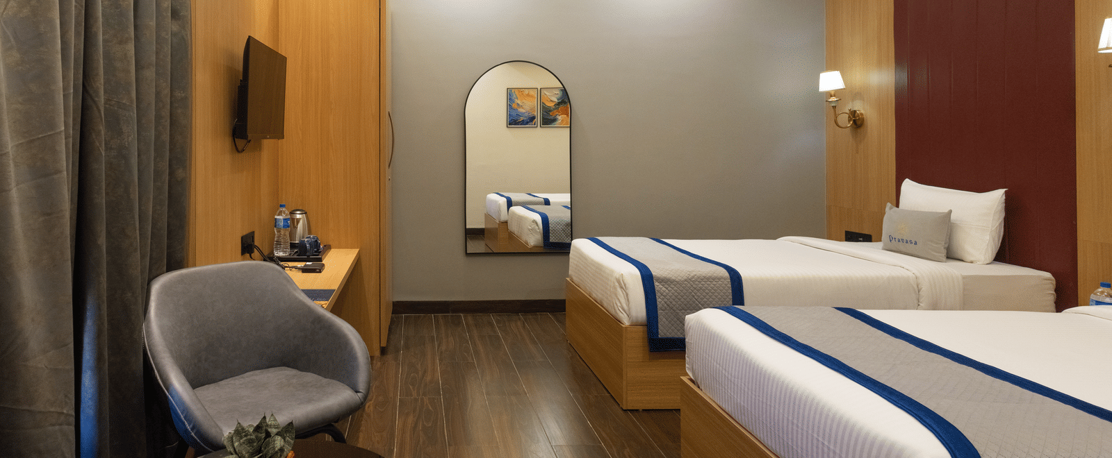 Interior of a guest room with 2 single beds, seating, and a rounded mirror at Pravasa Stay Luv Kush, Indore.