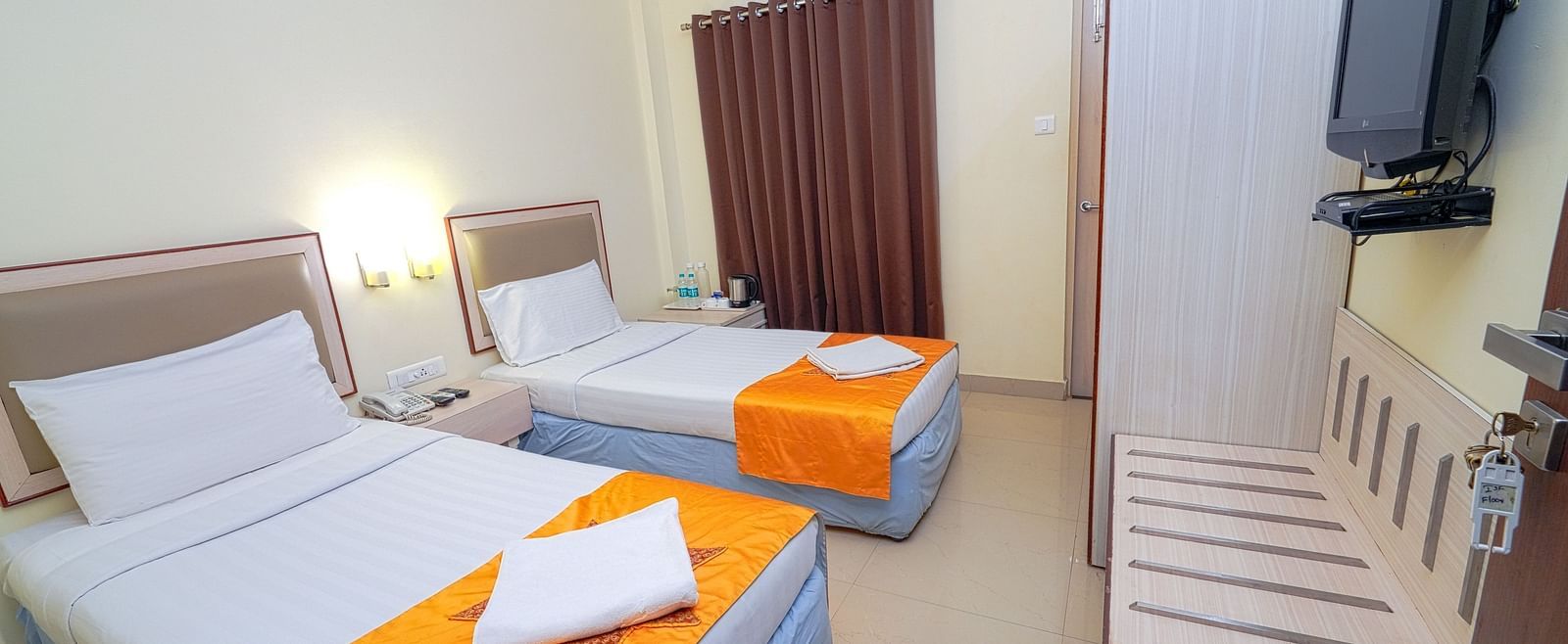A twin bedroom with light blue bedding, air conditioning, and a wall-mounted TV at Greens Inn - Cozy Accommodations in Ramoji Film City.