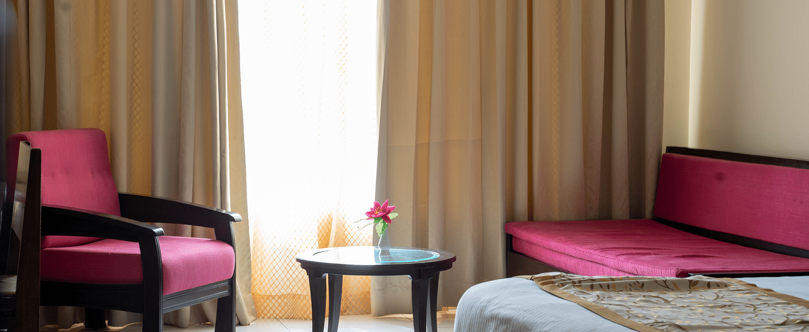 A hotel room with a seating area featuring two armchairs, a coffee table, and large windows with golden curtains - Hotel Udai Median, Udaipur.