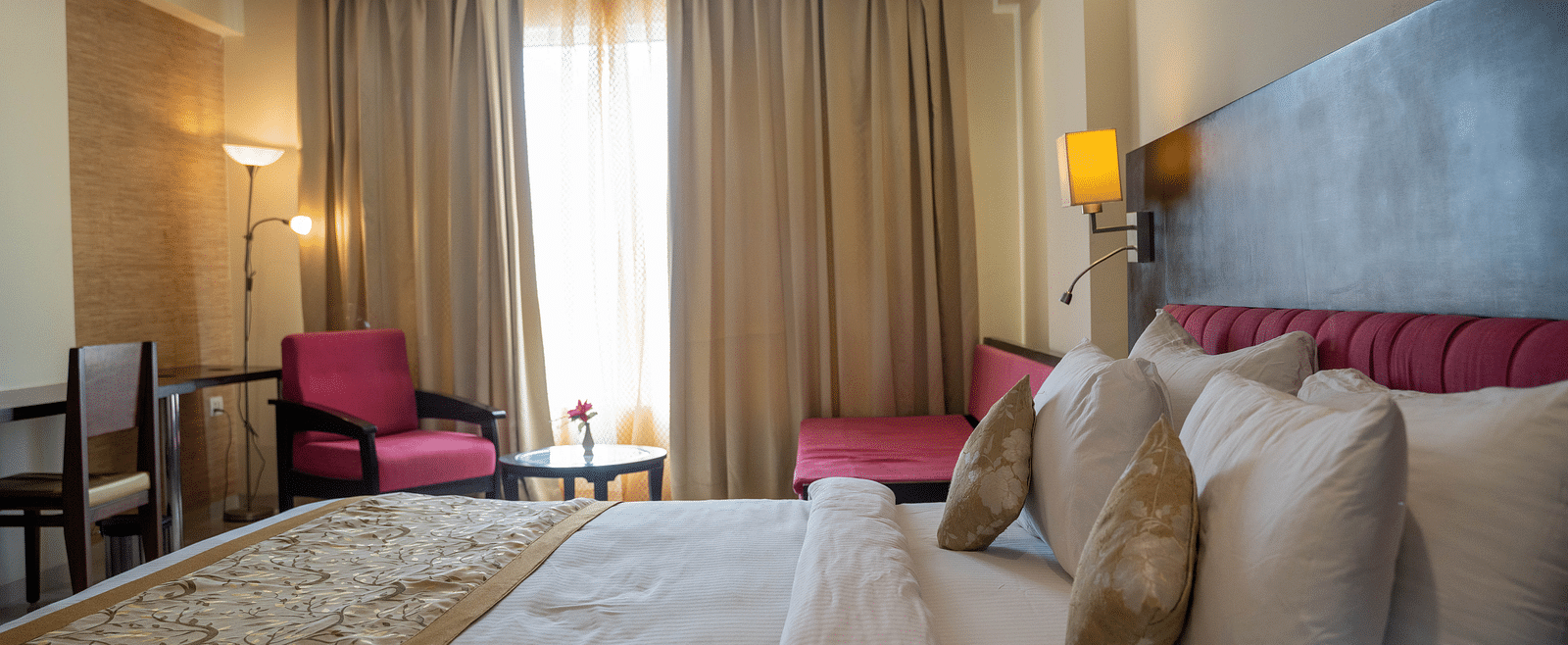 A spacious hotel room with a large bed, armchairs, and floor-to-ceiling curtains - Hotel Udai Median, Udaipur.