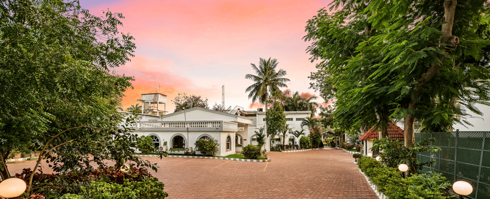 A facade image of GReaT Trails River View Resort Thanjavur By GRT Hotels surrounded by lush greenery