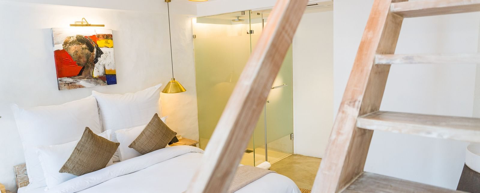 Deluxe loft room with a bed, bamboo lamps hung from the ceiling and art work on the wall - The Nanee