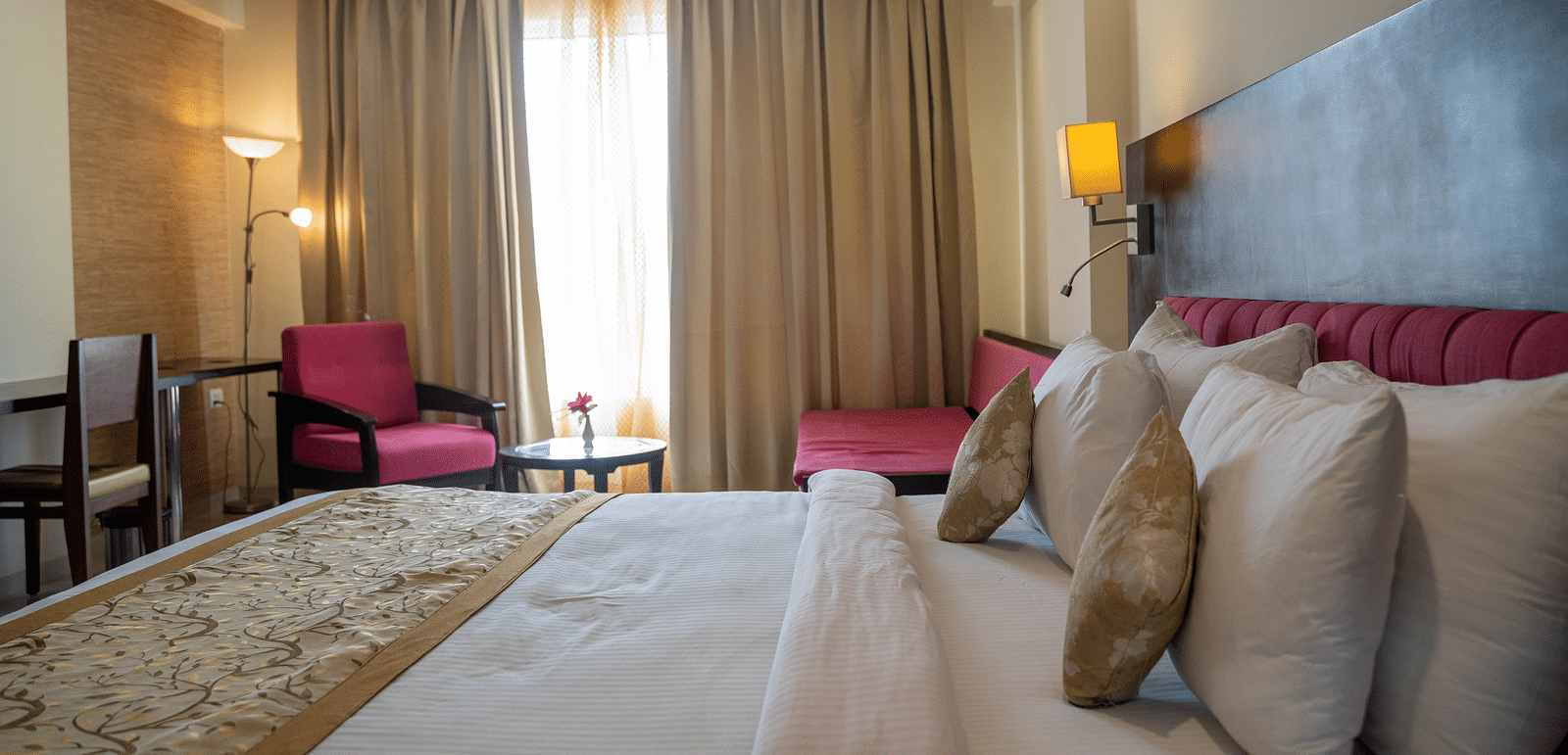 A spacious hotel room with a large bed, armchairs, and floor-to-ceiling curtains - Hotel Udai Median, Udaipur.
