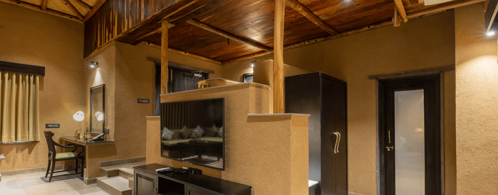 A spacious suite at Aamaghati Wildlife Resort with wooden ceilings, modern furniture, and elegant décor creating a warm ambience.