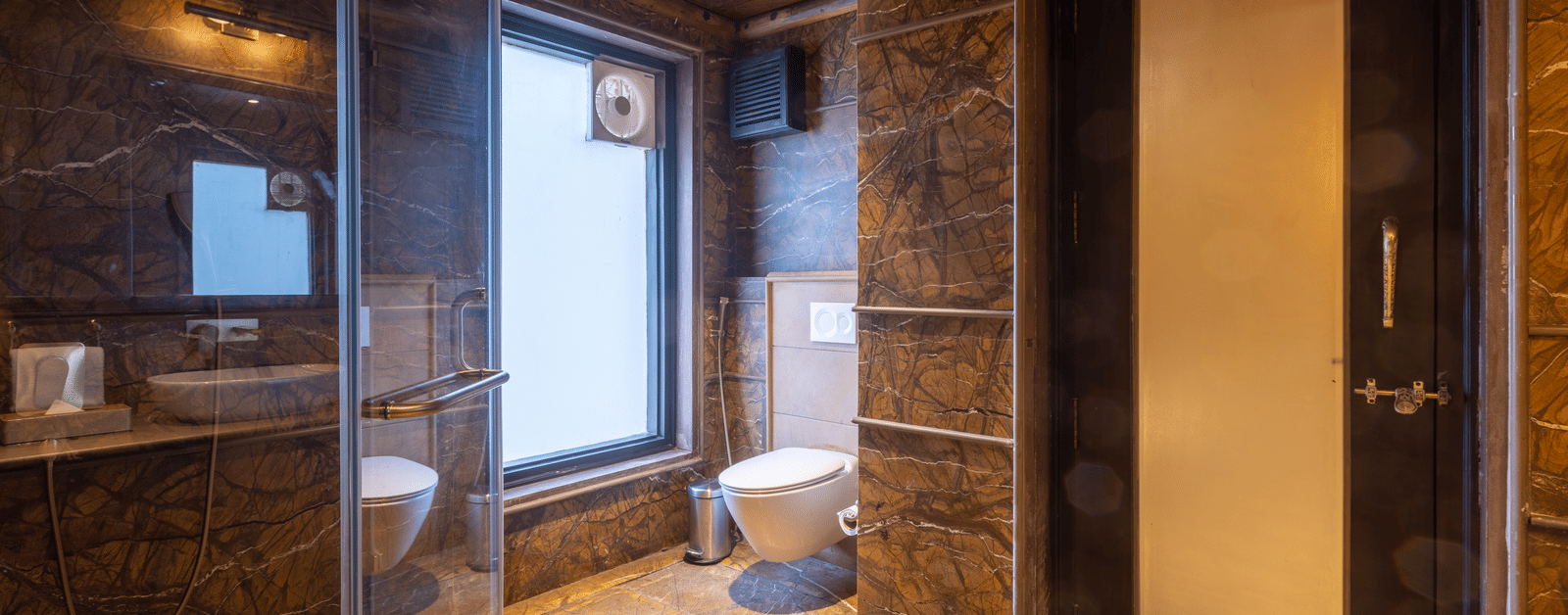 A luxurious bathroom at Aamaghati Wildlife Resort with stone walls, glass shower, and modern fittings designed for comfort.