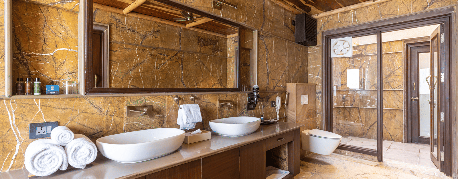 A modern bathroom at Aamaghati Wildlife Resort with twin basins, stone finishes, and soft lighting for a relaxing experience.