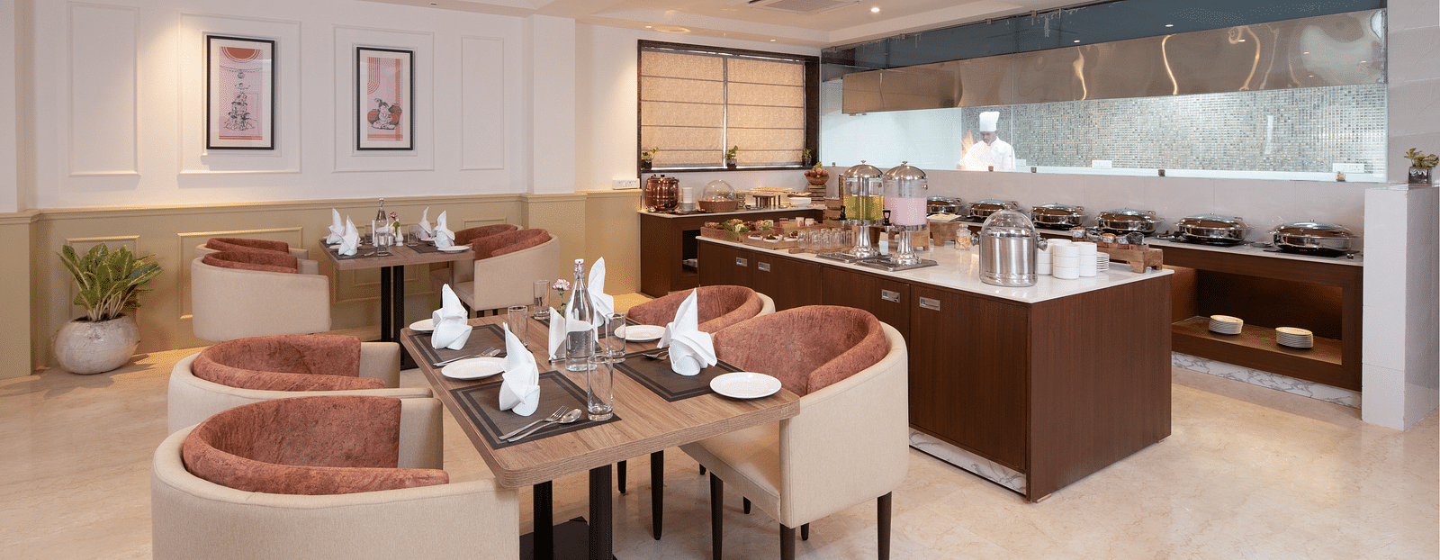 An image of a dining space with sofa chairs, centre table with hand towels and cutlery, and a buffet served at one corner - Brij Eternity, Vrindavan