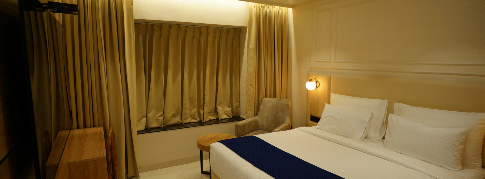  Cosy guest room at Monday Premium, Madhapur, featuring a double bed with a blue throw and a window with gold curtains.