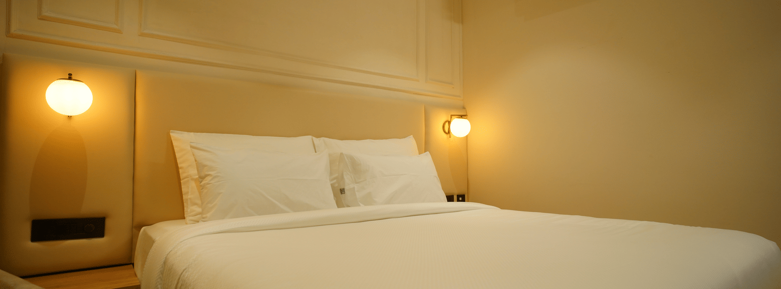  Close-up of a double bed at Monday Premium, Madhapur, showing crisp white linen, padded headboard, and warm bedside lighting.