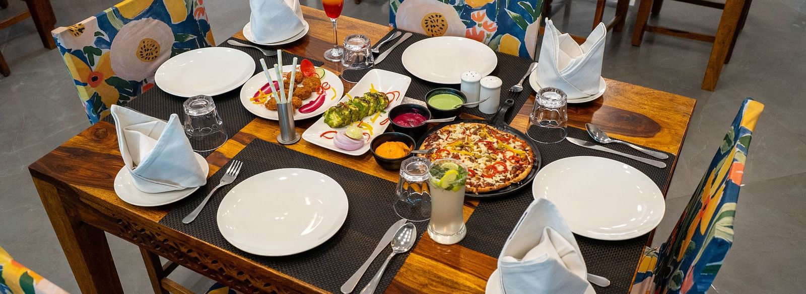 A neatly arranged food-filled dining table with cutlery and a spacious seating arrangement at the well-lit Bay Leaf Restaurant  in the Bamboo Saa Mulberry Resort in Pushkar.