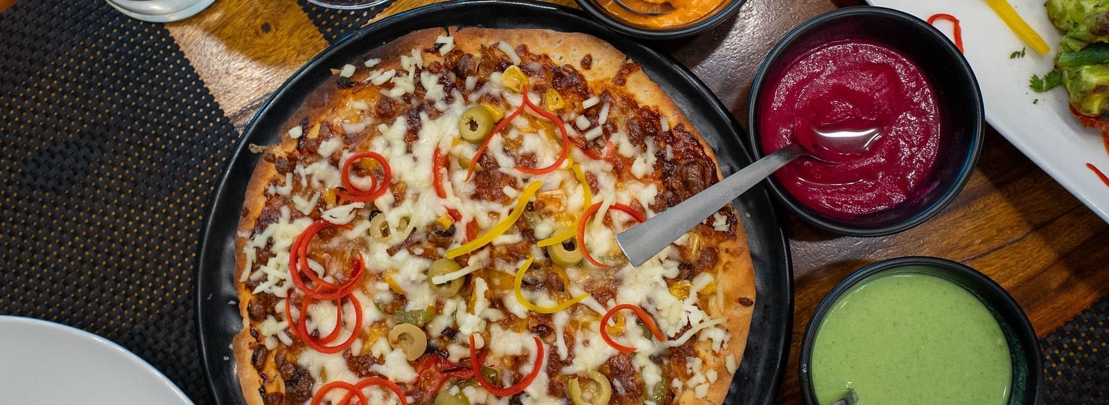 A food-filled table at the Bay Leaf Restaurant featuring a pizza with sauce and other condiments at Bamboo Saa Mulberry Resort in Pushkar.