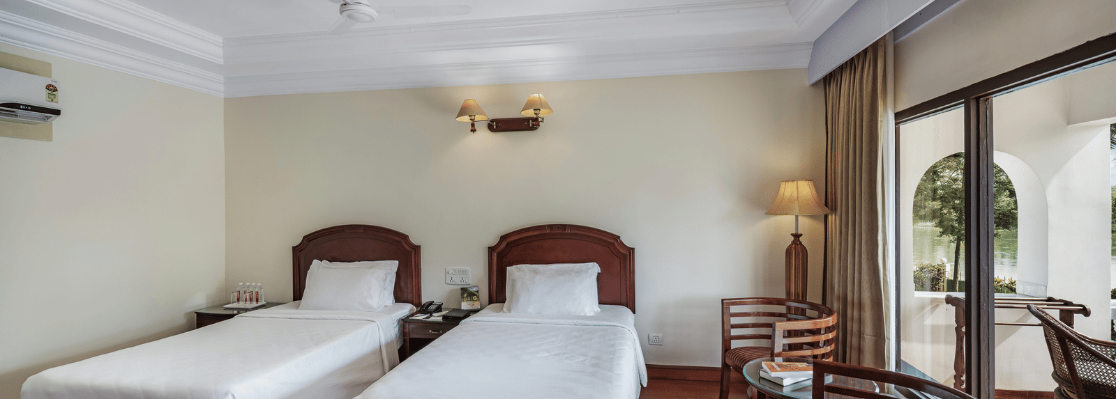 An image of the River View Room With Verandah featuring two single beds, bed side table, lamps, and chairs - GReaT Trails River View Resort Thanjavur By GRT Hotels