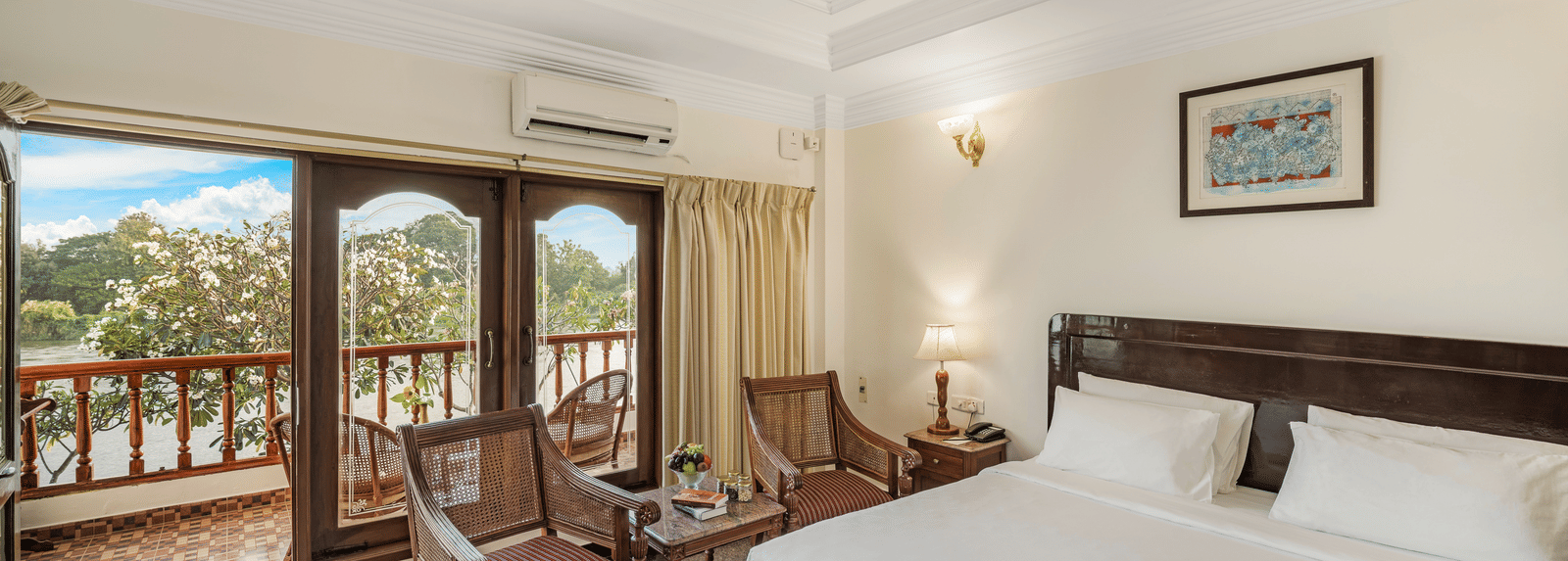 An image of the River Edge Heritage Room featuring a queen size bed, bed side table, lamps, and chairs - GReaT Trails River View Resort Thanjavur By GRT Hotels