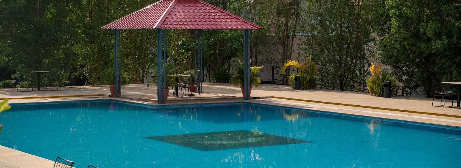 An open gazebo by the outdoor pool canopied by trees at Bamboo Saa Mulberry Resort, Pushkar on a sunny morning.