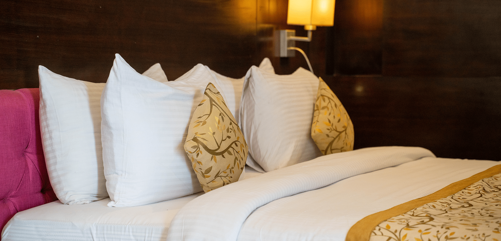 A luxurious hotel bed with plush pillows, gold-accented linens, and ambient lighting - Hotel Udai Median, Udaipur.