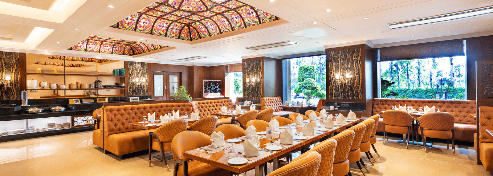 Long view of the spacious restaurant with multiple dining tables, comfortable seating, and a view of the outside through windows at Hotel Hukam's Lalit Mahal.