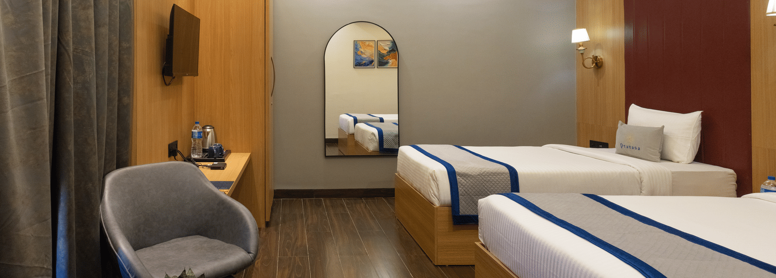 Interior of a guest room with 2 single beds, seating, and a rounded mirror at Pravasa Stay Luv Kush, Indore.