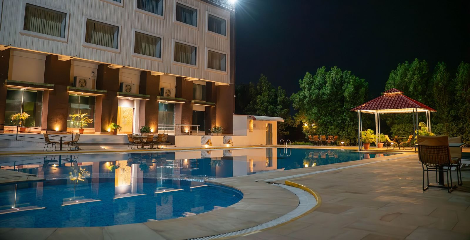 Bamboo Saa Mulberry Resort in Pushkar standing tall beside the outdoor swimming pool at night featuring warm lighting and an open gazebo. 