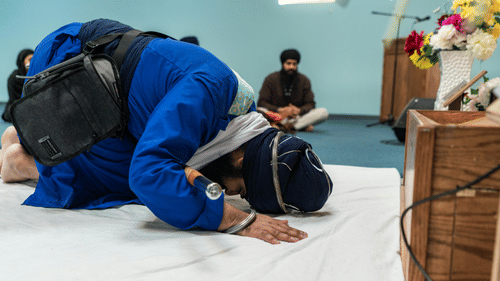 A devotee in blue traditional attire bowing in prayer on a white floor inside a religious shrine at Ananta Express, Katra.