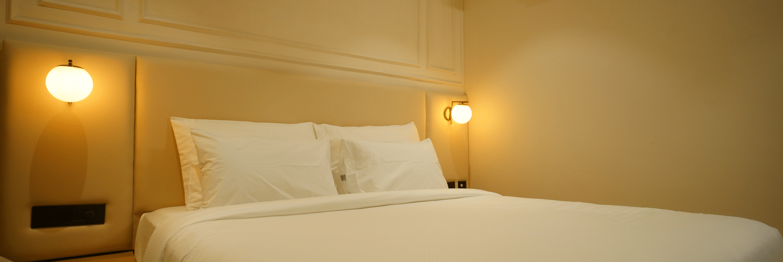  Close-up of a double bed at Monday Premium, Madhapur, showing crisp white linen, padded headboard, and warm bedside lighting.