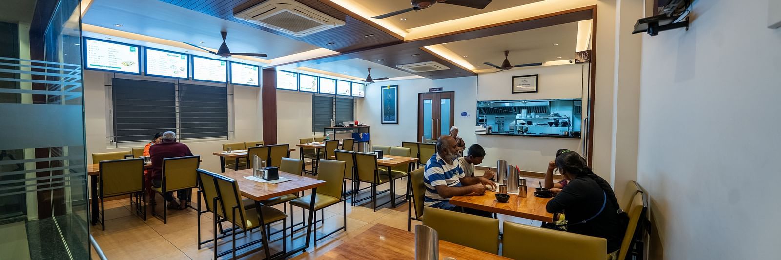 Diagonal view of the dining area at Hari Govinda's, with a neatly arranged table and chairs, and lighting featured in the ceiling corner