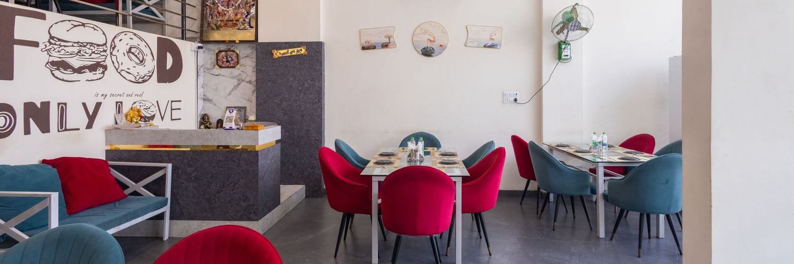 Dining area with red and blue chairs, tables, and wall art at Pravasa Stay Dewas Naka, Indore.