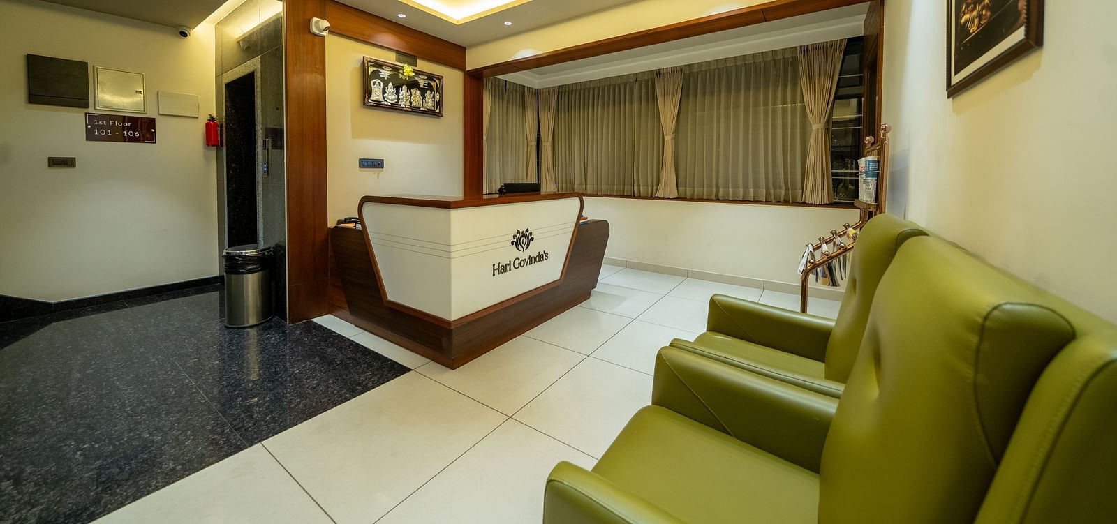 Reception area at Hari Govinda's Express, Vijayanagar, features a desk at one end, cushioned sofas directly opposite, and a photo frame above them.