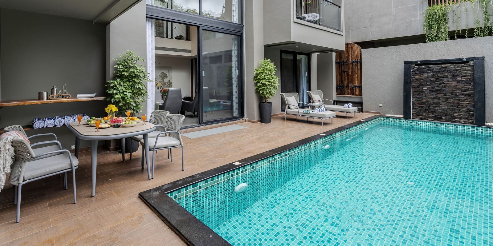 Corner view of the pool at Lindsay Manor, featuring a seating area with a table and chairs, and the exterior of the living area.