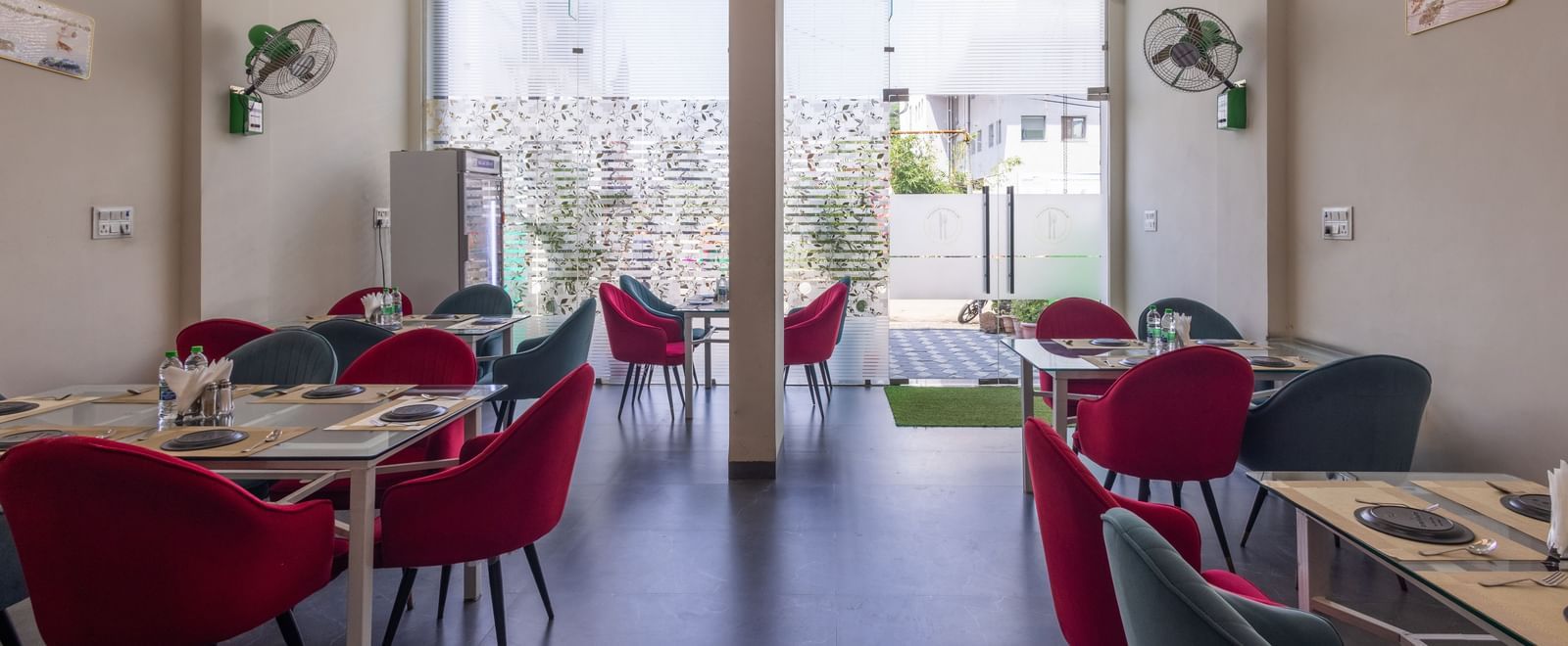 Bright dining hall with glass doors, tables, and red chairs at Pravasa Stay Dewas Naka, Indore.
