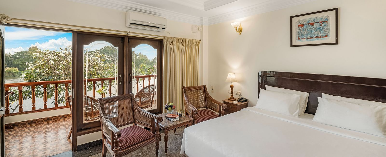 An image of the River Edge Heritage Room featuring a queen size bed, bed side table, lamps, and chairs - GReaT Trails River View Resort Thanjavur By GRT Hotels