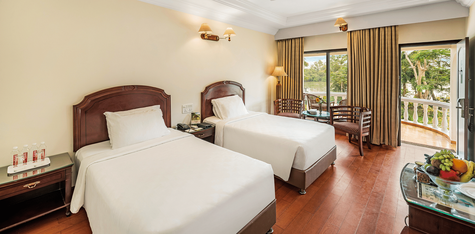 An image of the River View Room With Verandah featuring two single beds, bed side table, lamps, flat screen TV, and chairs - GReaT Trails River View Resort Thanjavur By GRT Hotels