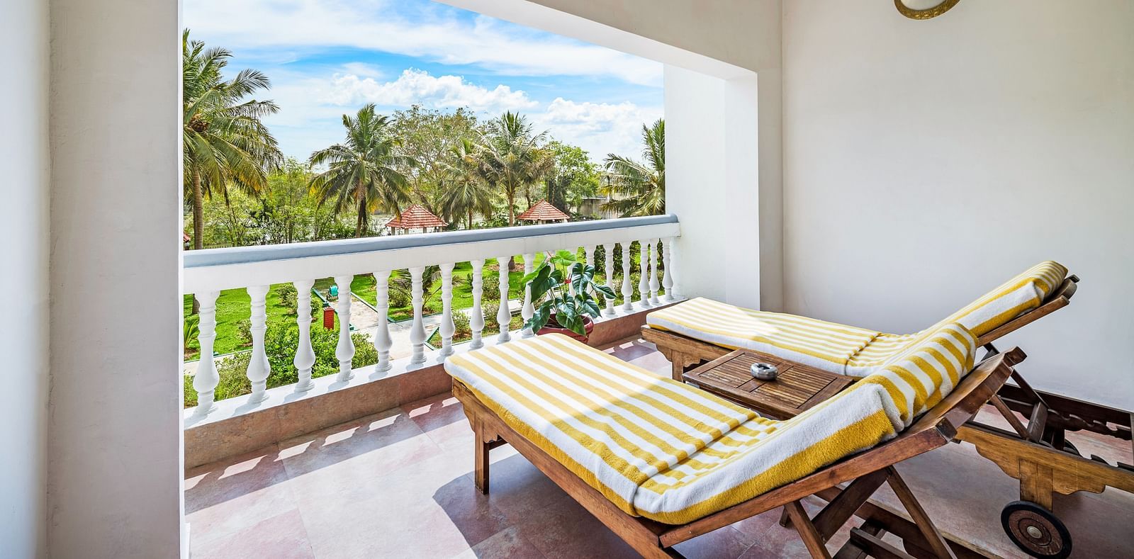 An image of a balcony of the Garden room with river view featuring two lounge chairs over viewing the lush greenery and the river - GReaT Trails River View Resort Thanjavur By GRT Hotels