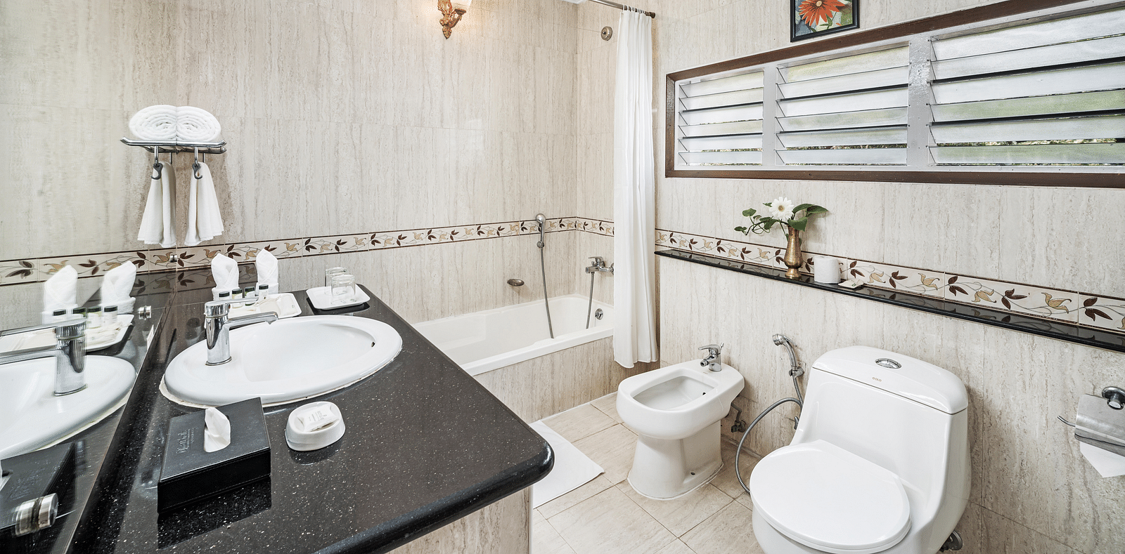 An image of a washroom showcasing a big mirror, along with toiletries and the washroom is brightly lit - GReaT Trails River View Resort Thanjavur By GRT Hotels