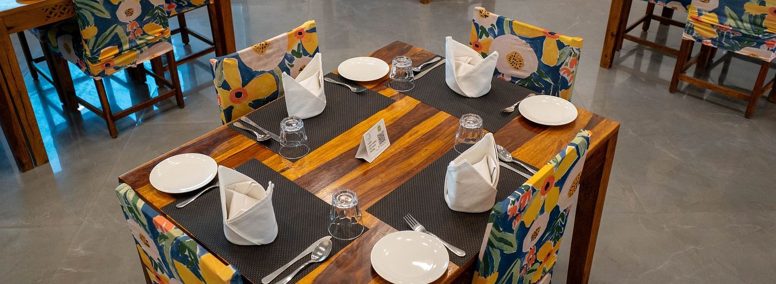 A neatly arranged table with cutlery and a spacious seating arrangement at the well-lit Bay Leaf Restaurant  in the Bamboo Saa Mulberry Resort in Pushkar.