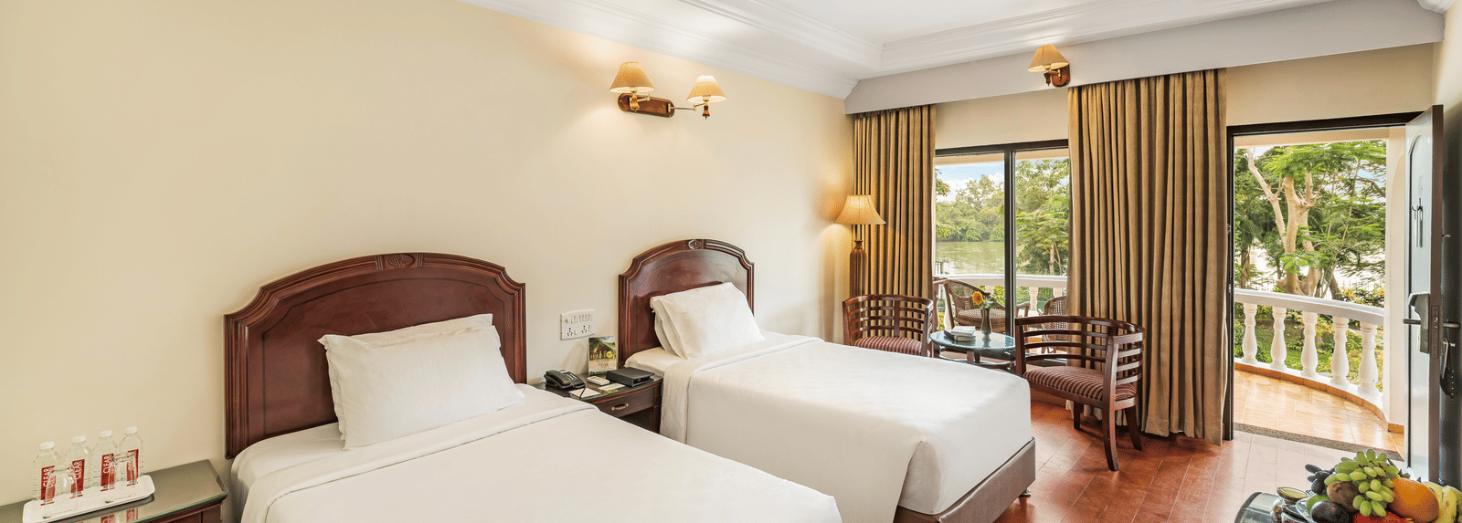 An image of the River View Room With Verandah featuring two single beds, bed side table, lamps, flat screen TV, and chairs - GReaT Trails River View Resort Thanjavur By GRT Hotels