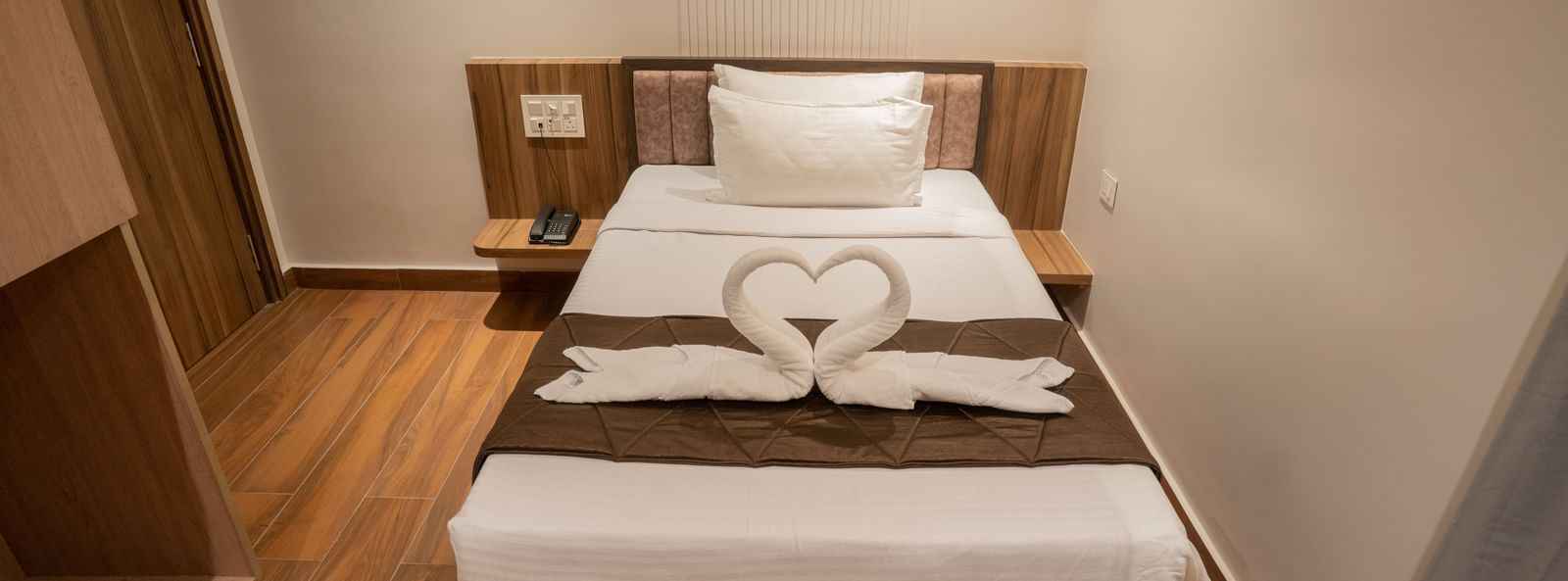 Single bed with crisp linen and towel swan decoration creating a warm ambience at Beestay Hotels, Rajahmundry.
