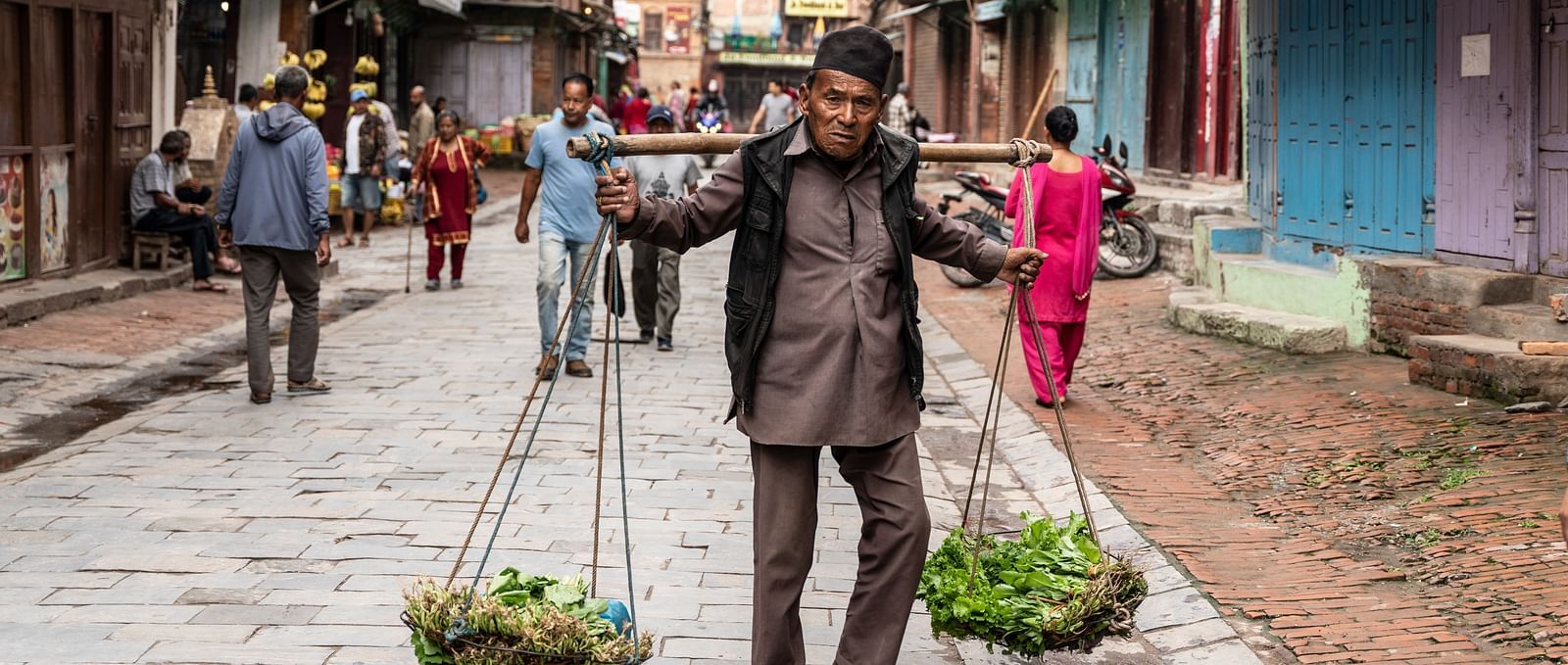 A man carrying vegetables on bamboo baskets attached to a pole