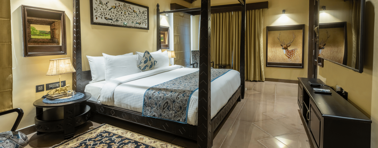 A spacious bedroom at Aamaghati Wildlife Resort with a four poster bed, elegant décor, and warm lighting creating a cosy and inviting atmosphere.
