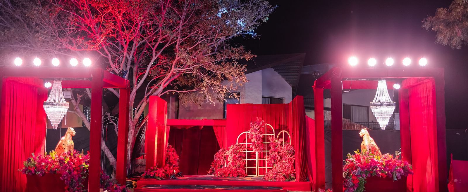 A stage is dramatically lit in red, flanked by trees and decorative elements | The Qualia Resort Club & Brewery, Udaipur