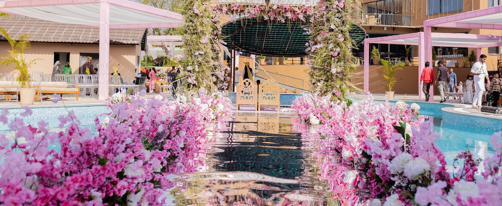 An outdoor venue showcases floral decor around a pool area and buildings | The Qualia Resort Club & Brewery, Udaipur