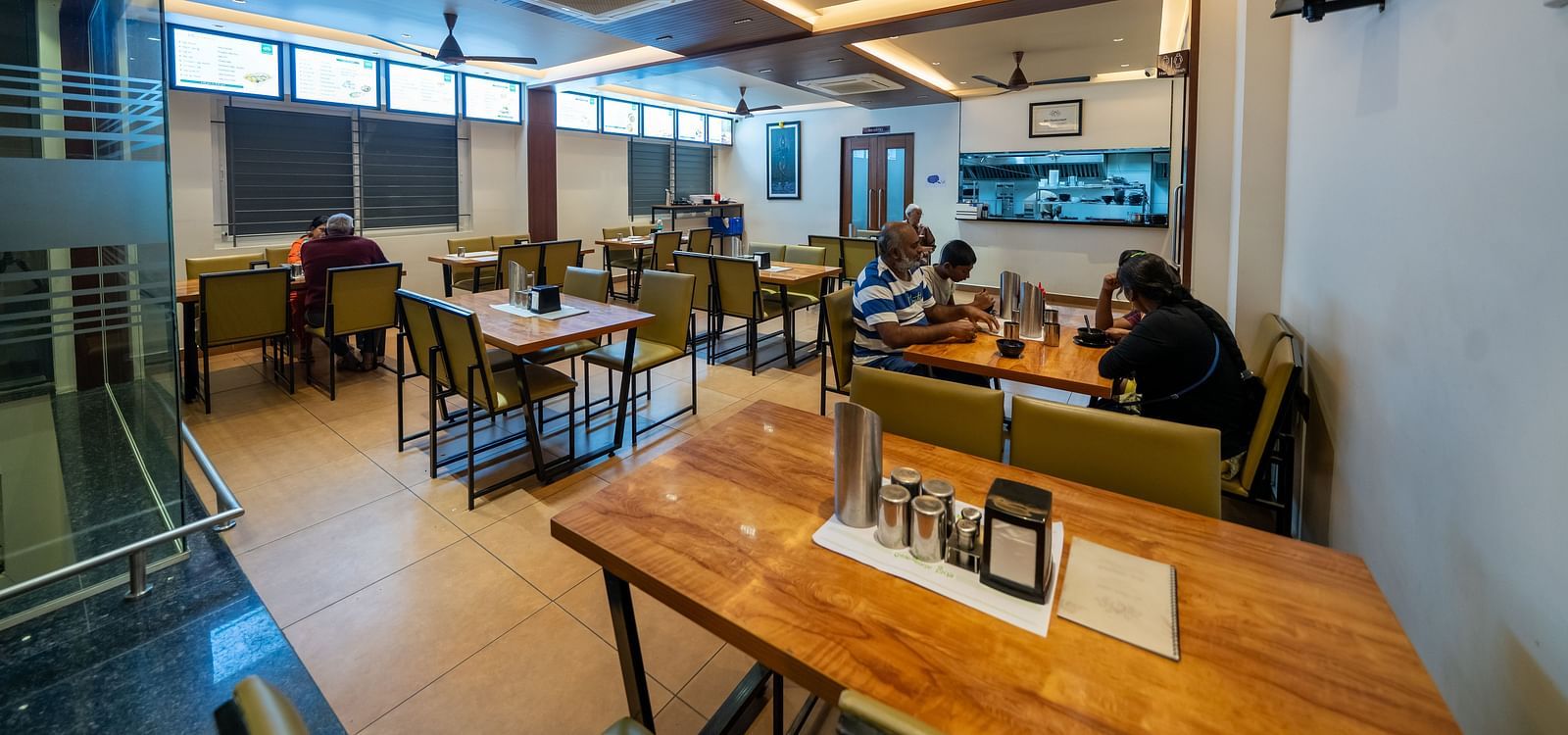 Diagonal view of the dining area at Hari Govinda's, with a neatly arranged table and chairs, and lighting featured in the ceiling corner
