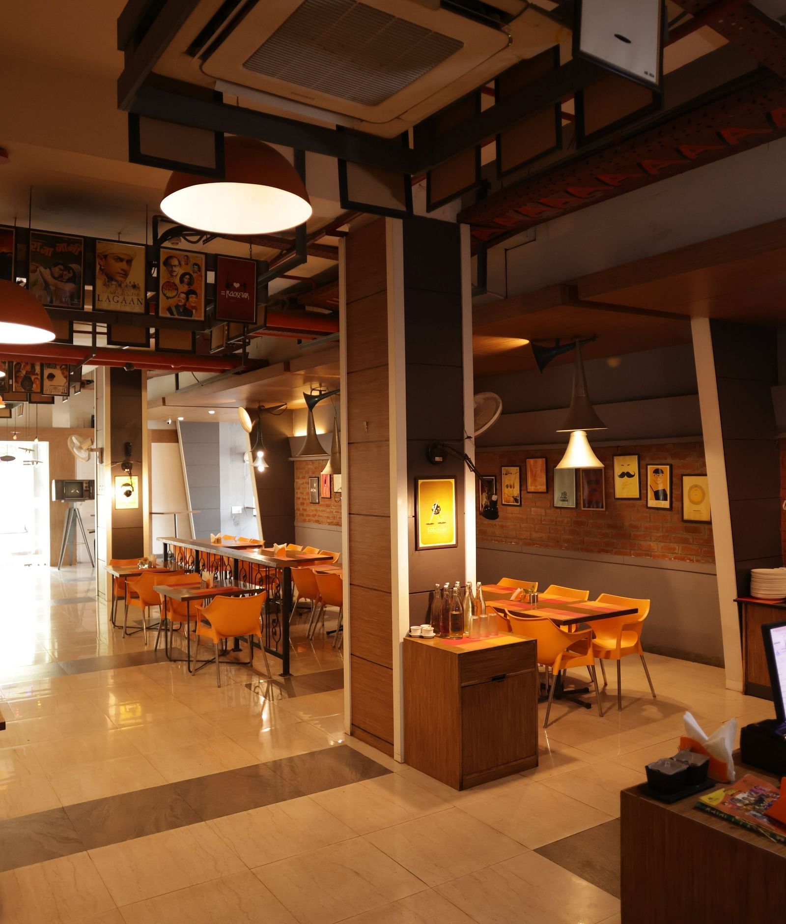 A warmly lit interior of Mumbai Masala Restaurant with wooden furniture, a laptop on a counter at Max Hotel Prayagraj.