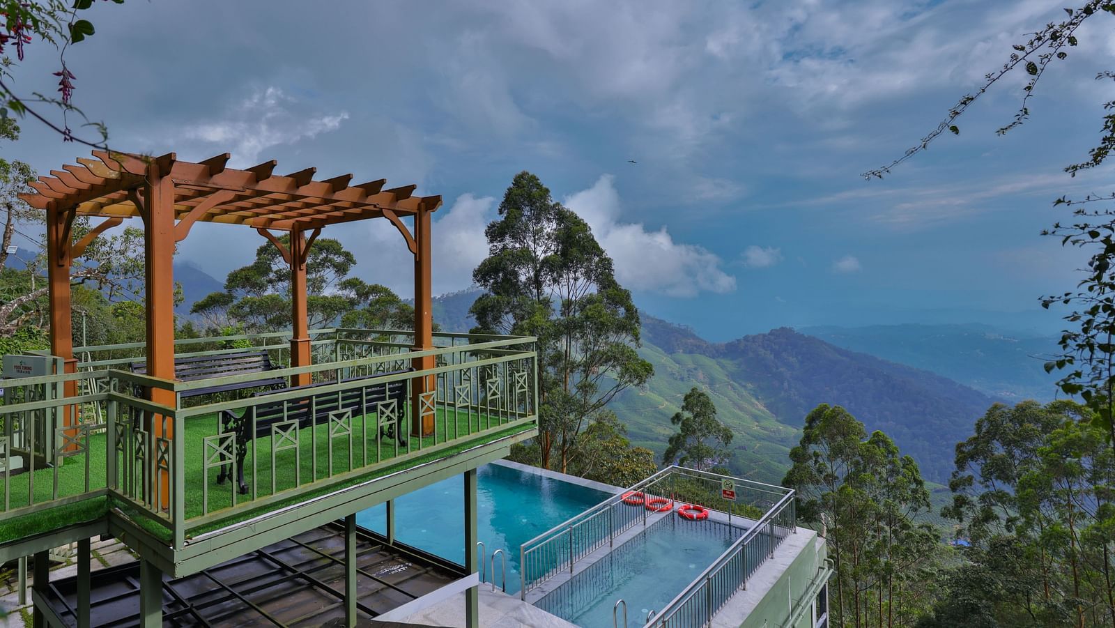 Balcony with a view of the ground-floor swimming pool, surrounded by trees and hills - Fragrant Nature Munnar