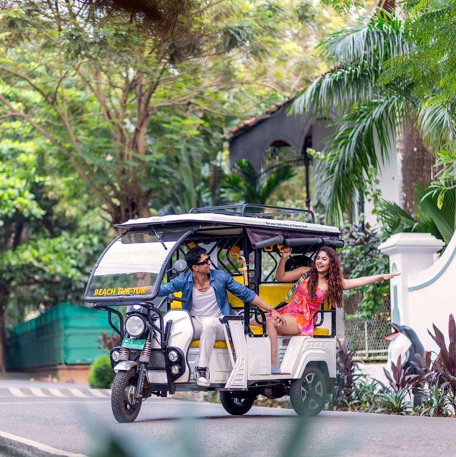 Colourful tuk-tuk parked under lush trees at a tropical resort entrance.