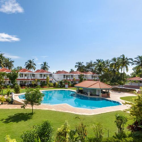 A view of the Poolside Lawn with a swimming pool, a spacious green garden, and large trees surrounding the area - Heritage Village Resorts & Spa