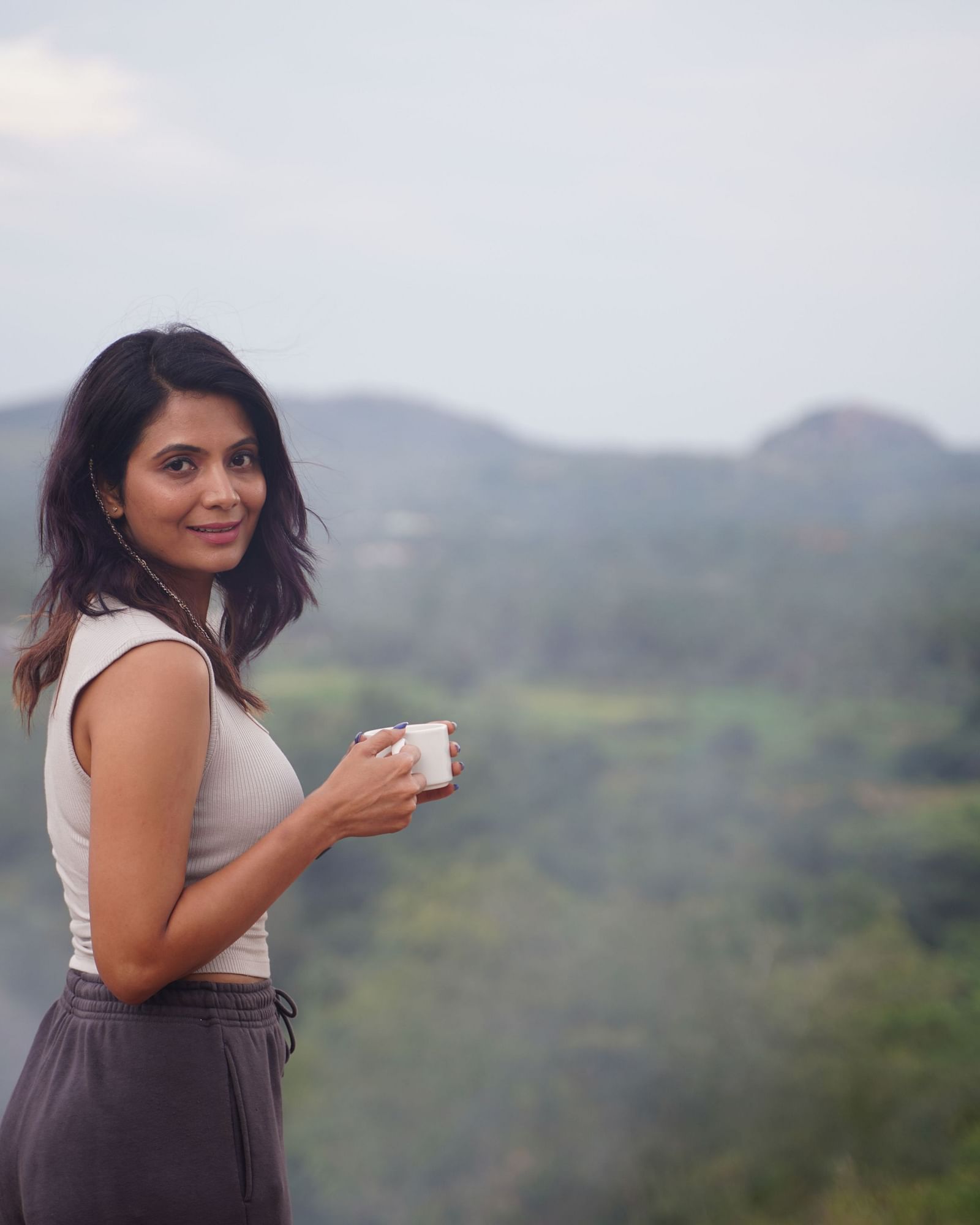 Ravishing Retreat Ramanagara - A guest holding a coffee mug in her hand with a lush green view in the backdrop