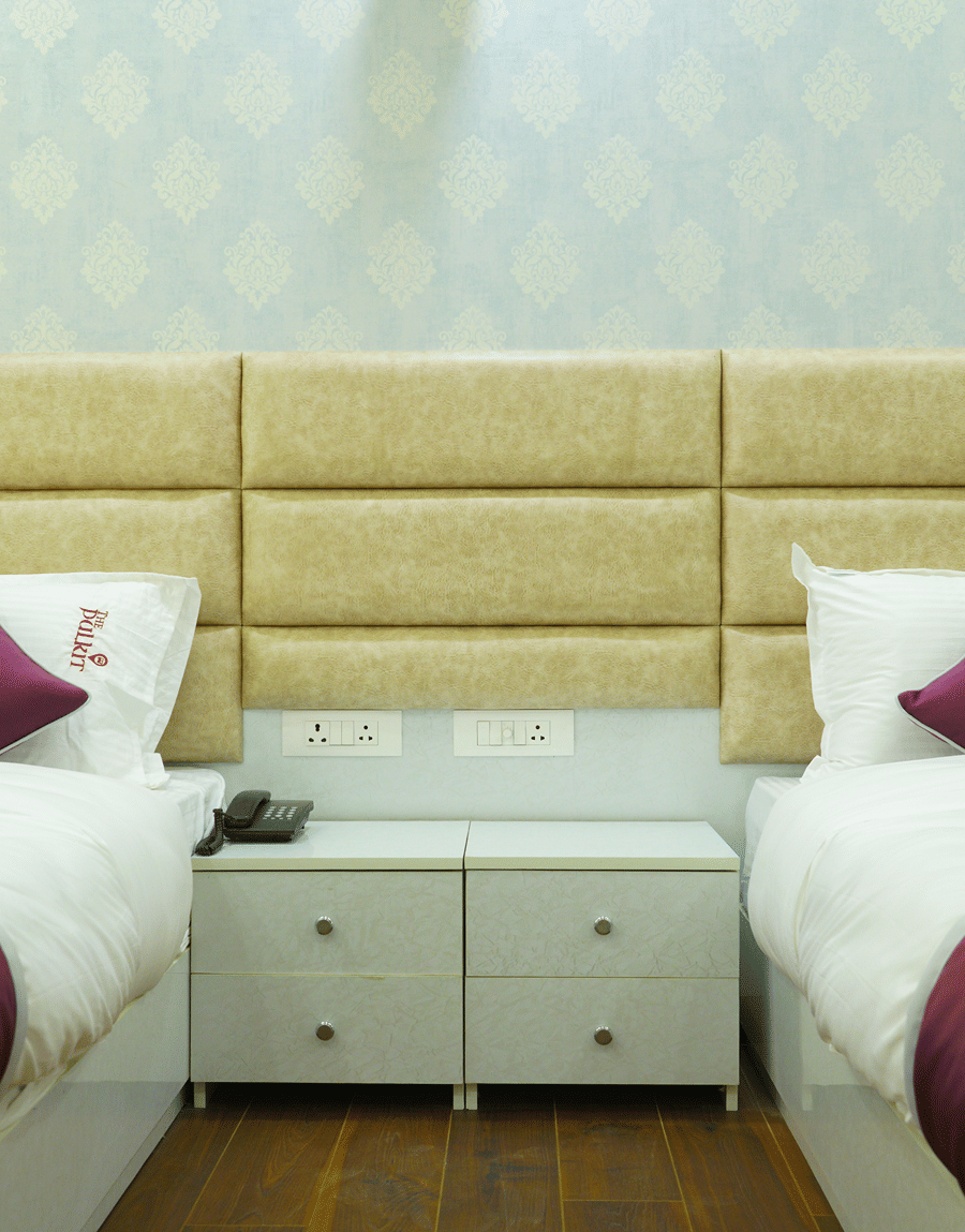Twin beds with a padded beige headboard and bedside drawers in the Deluxe Room with Balcony at Lime Tree Hotel, Pulkit