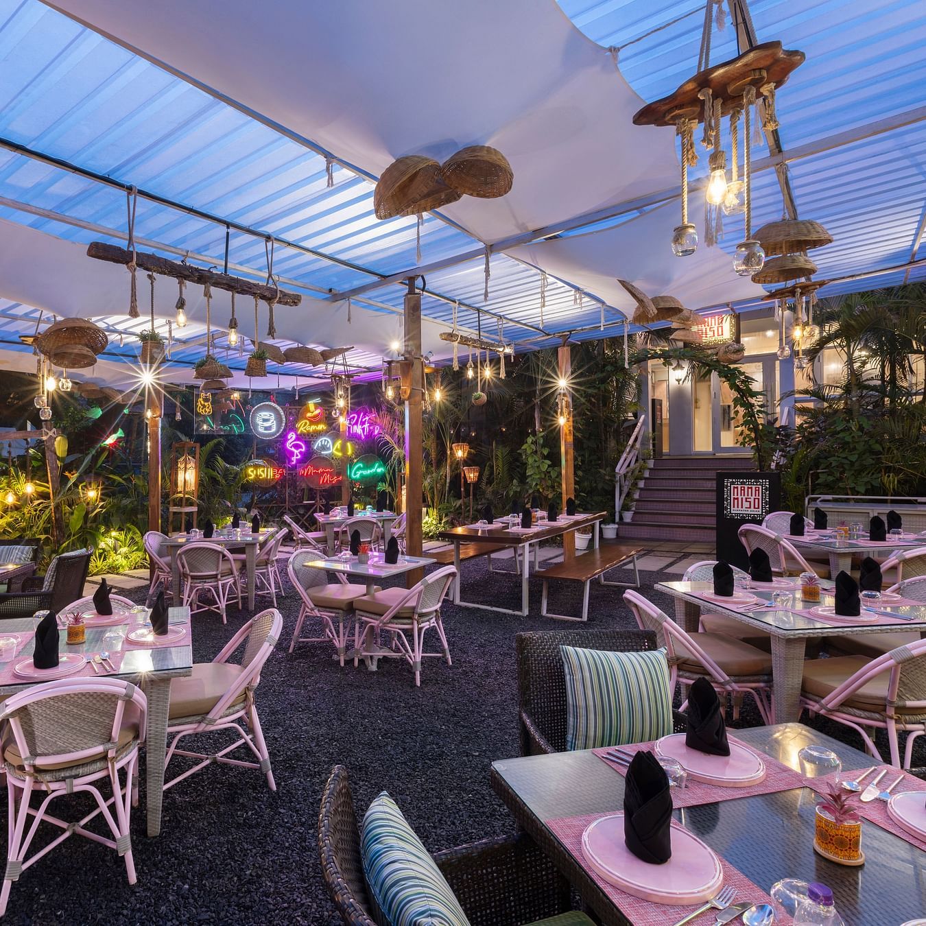 Evening view of a covered outdoor dining area with warm lighting and garden ambience.