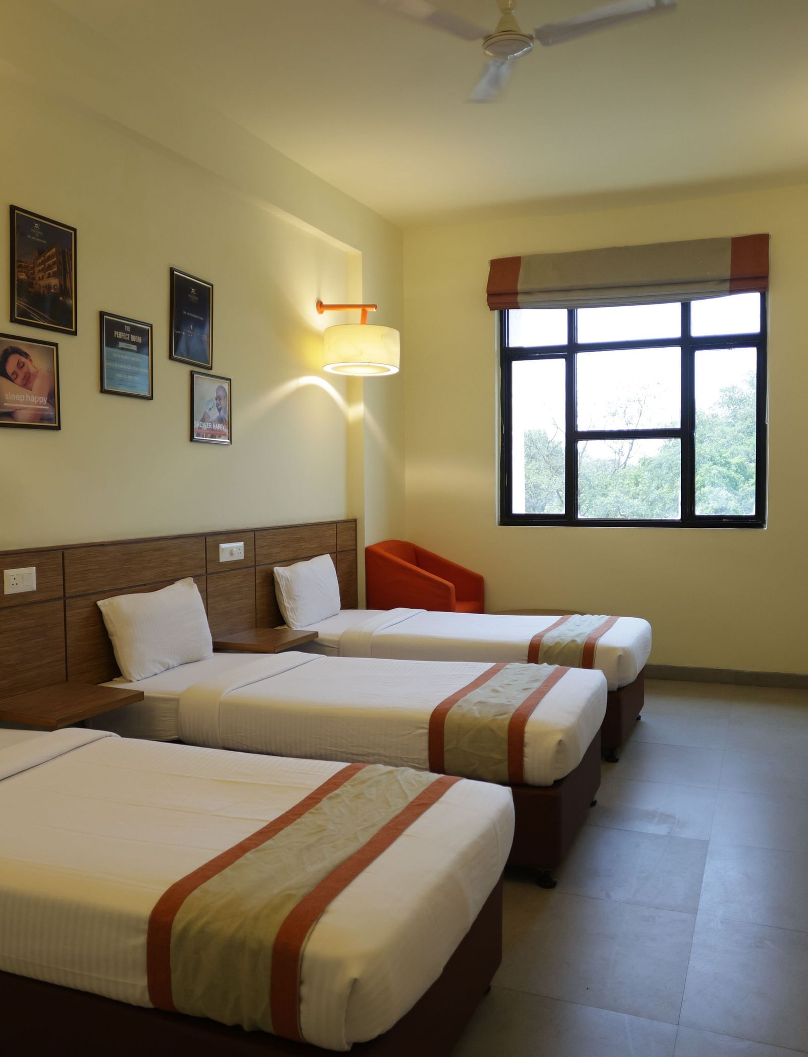 a neatly kept room with three comfortable single beds with small photo frames hung on the wall behind them - Max Hotel Jabalpur