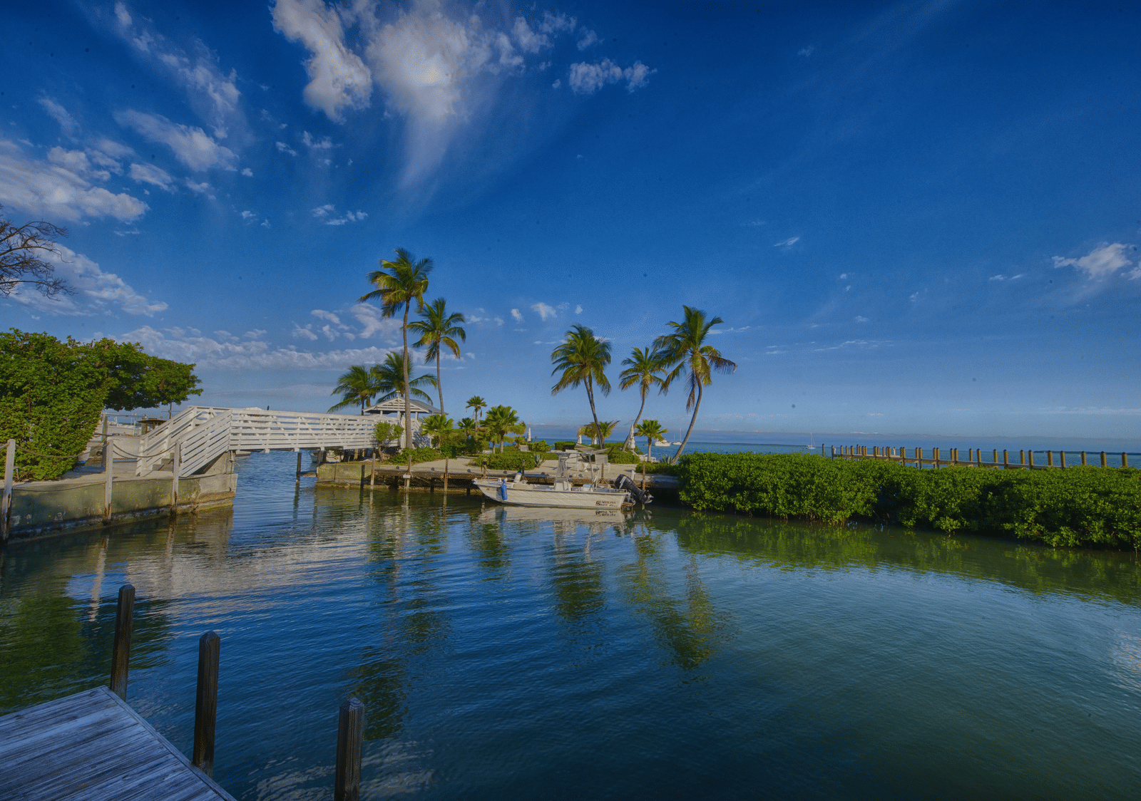 A wooden over bridge going over a calm water body featuring the reflection of the surrounding greenery and the clear blue sky at the top at Casa Morada.